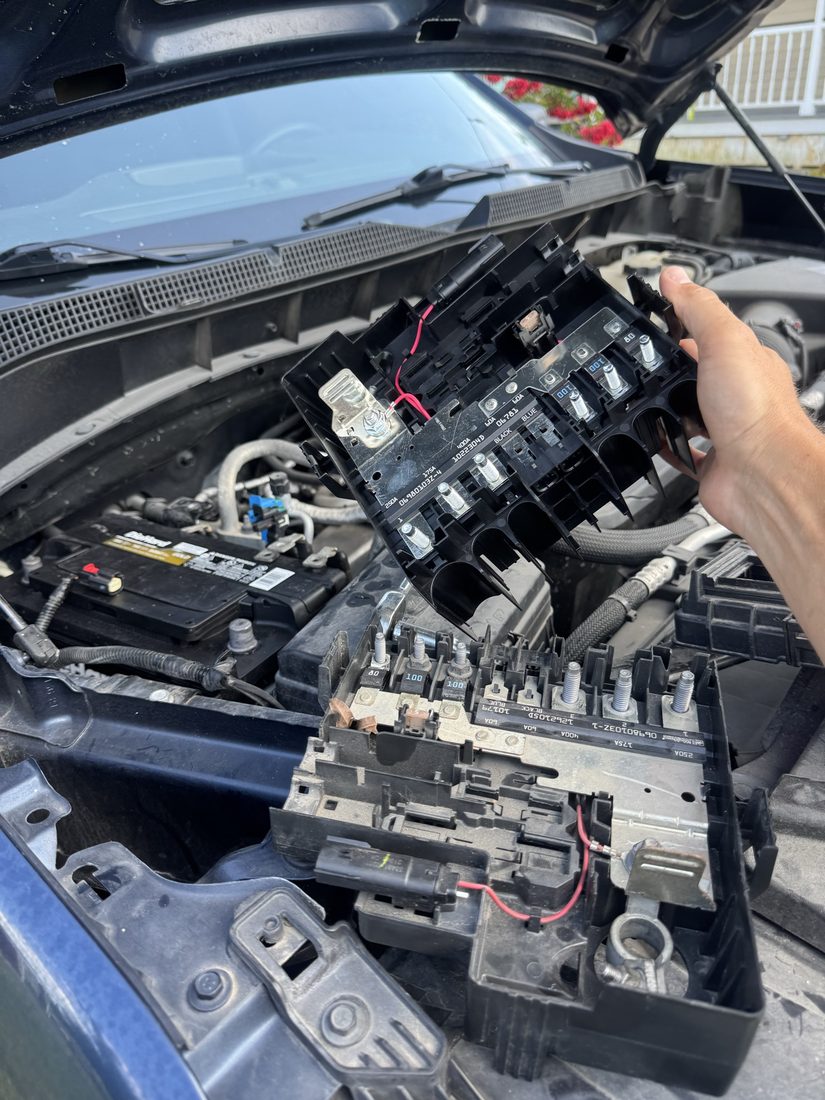 Hand holding an electrical distribution block over a vehicle battery during diagnosis