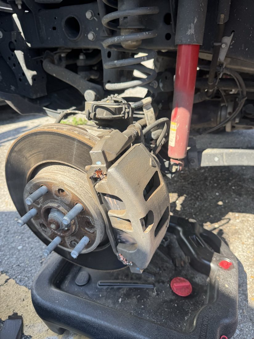 Exposed brake rotor and caliper assembly over a drain pan during brake service
